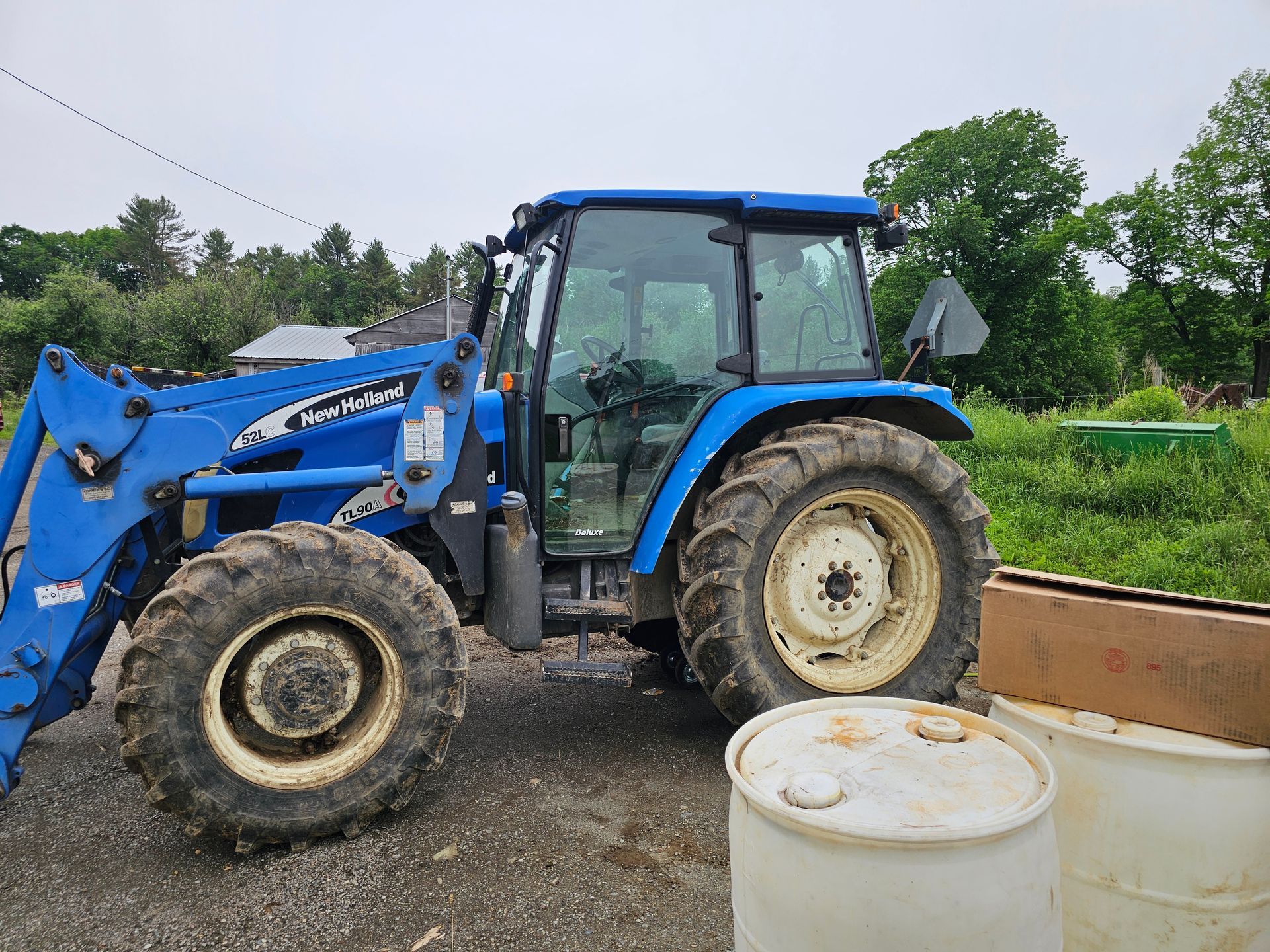 A blue tractor is parked next to two white barrels.