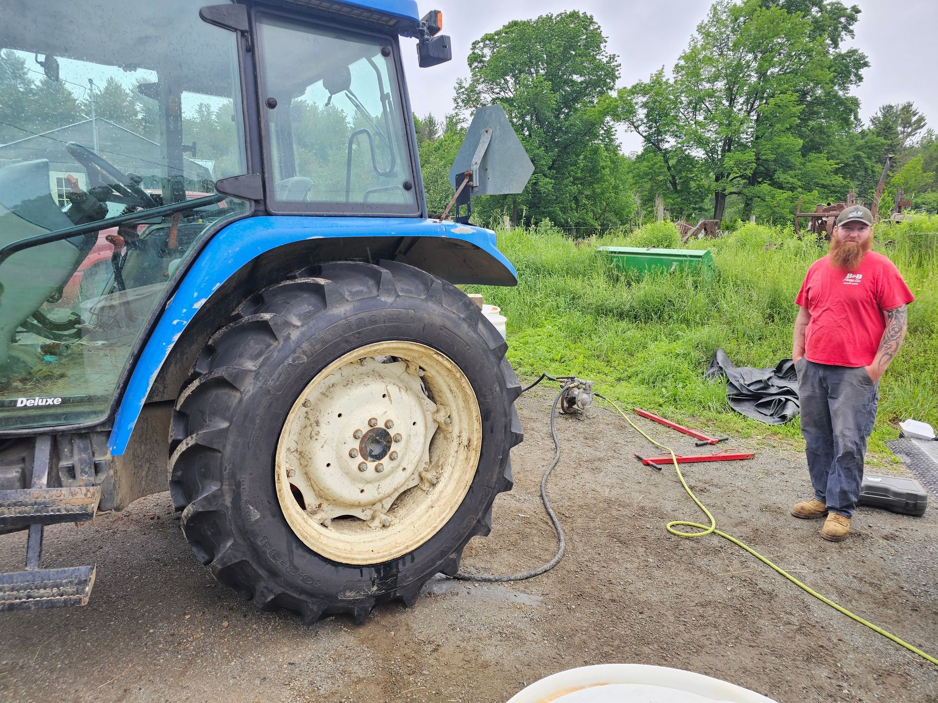 A man in a red shirt is standing next to a blue tractor.