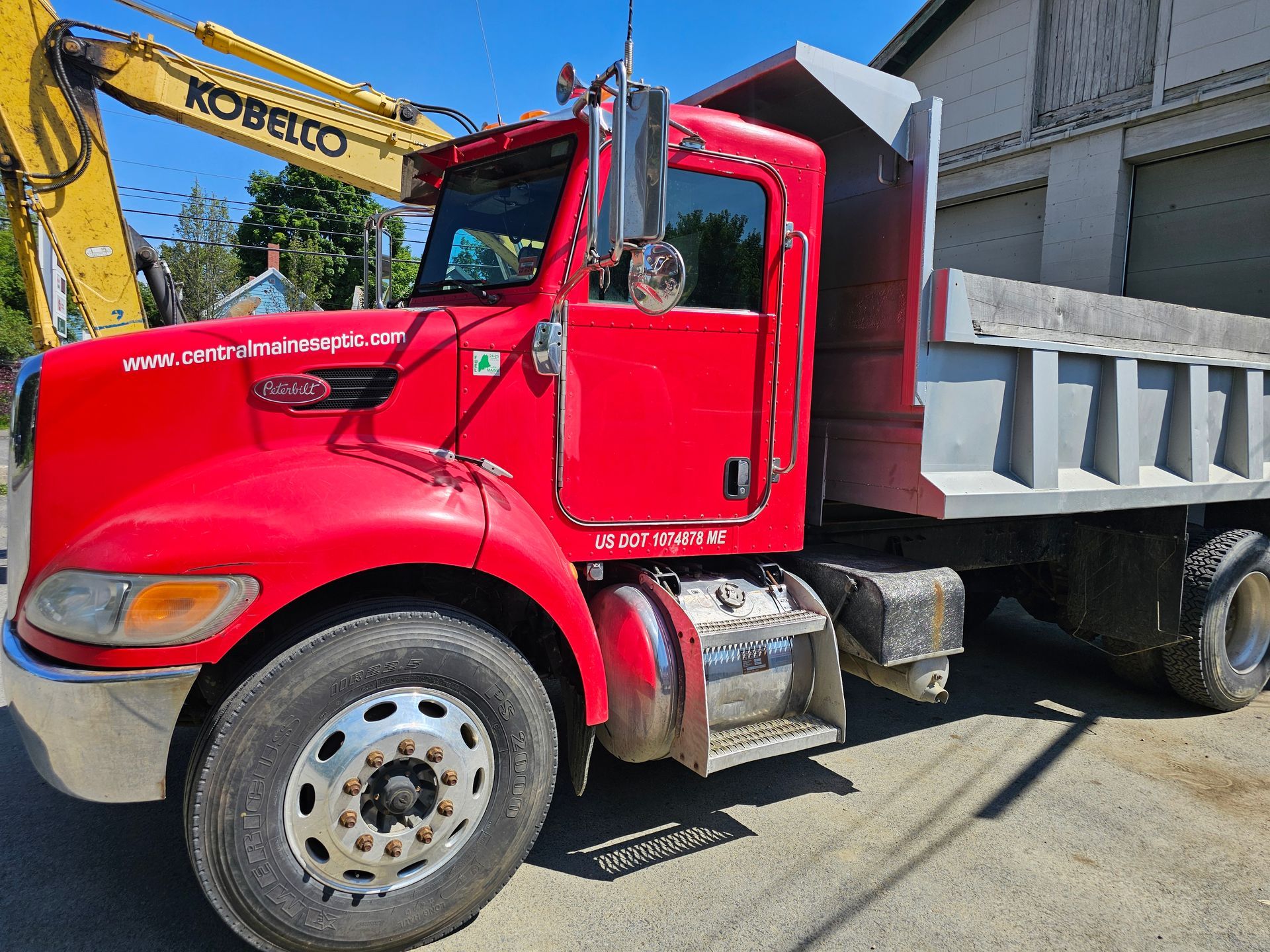 A red dump truck is parked next to a yellow kobelco excavator