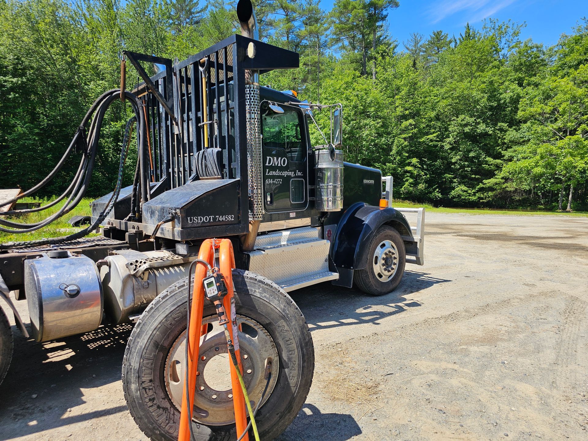 A large truck is parked in a dirt lot with trees in the background.