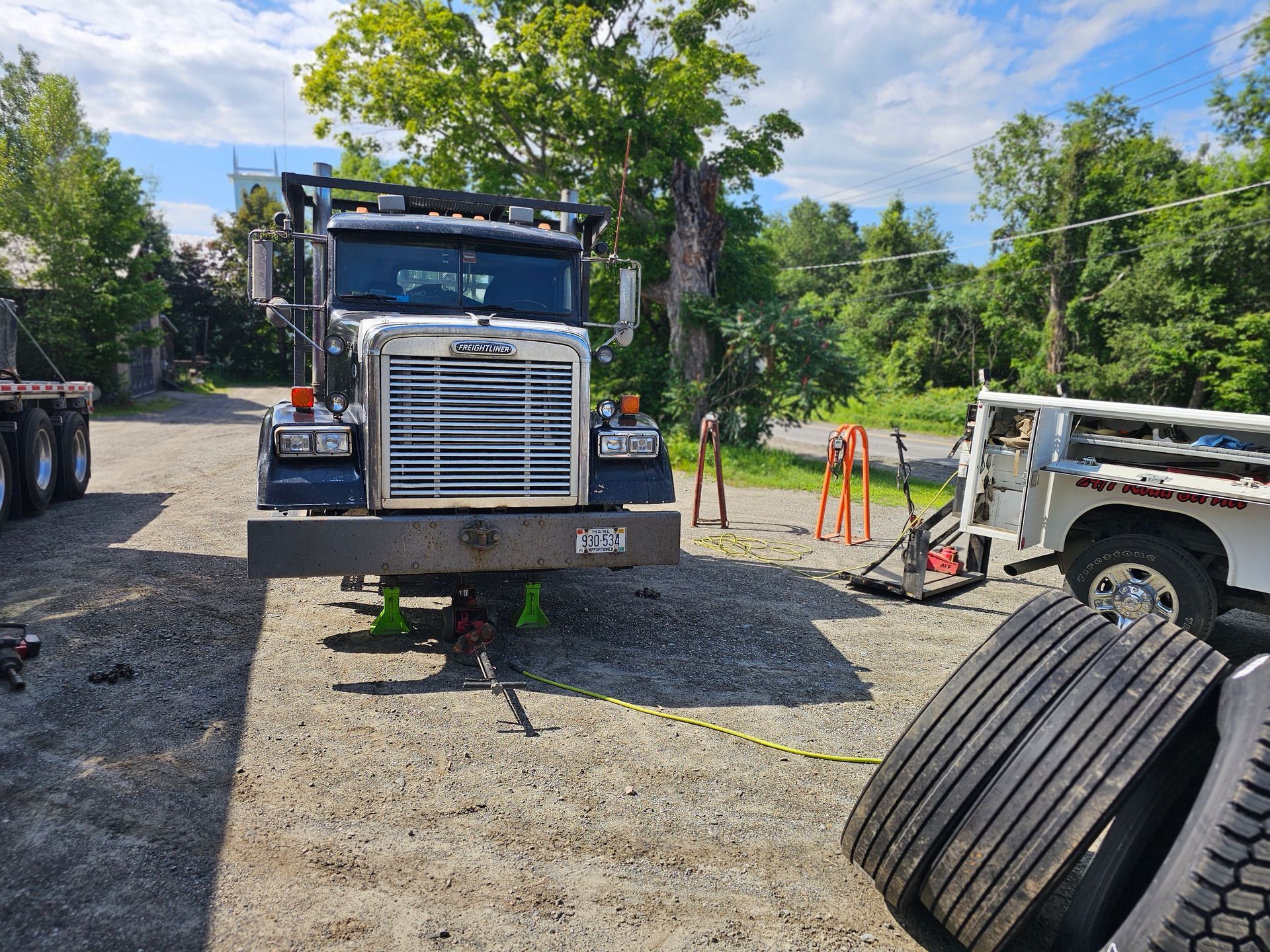 A truck is sitting in a gravel lot next to a pile of tires.