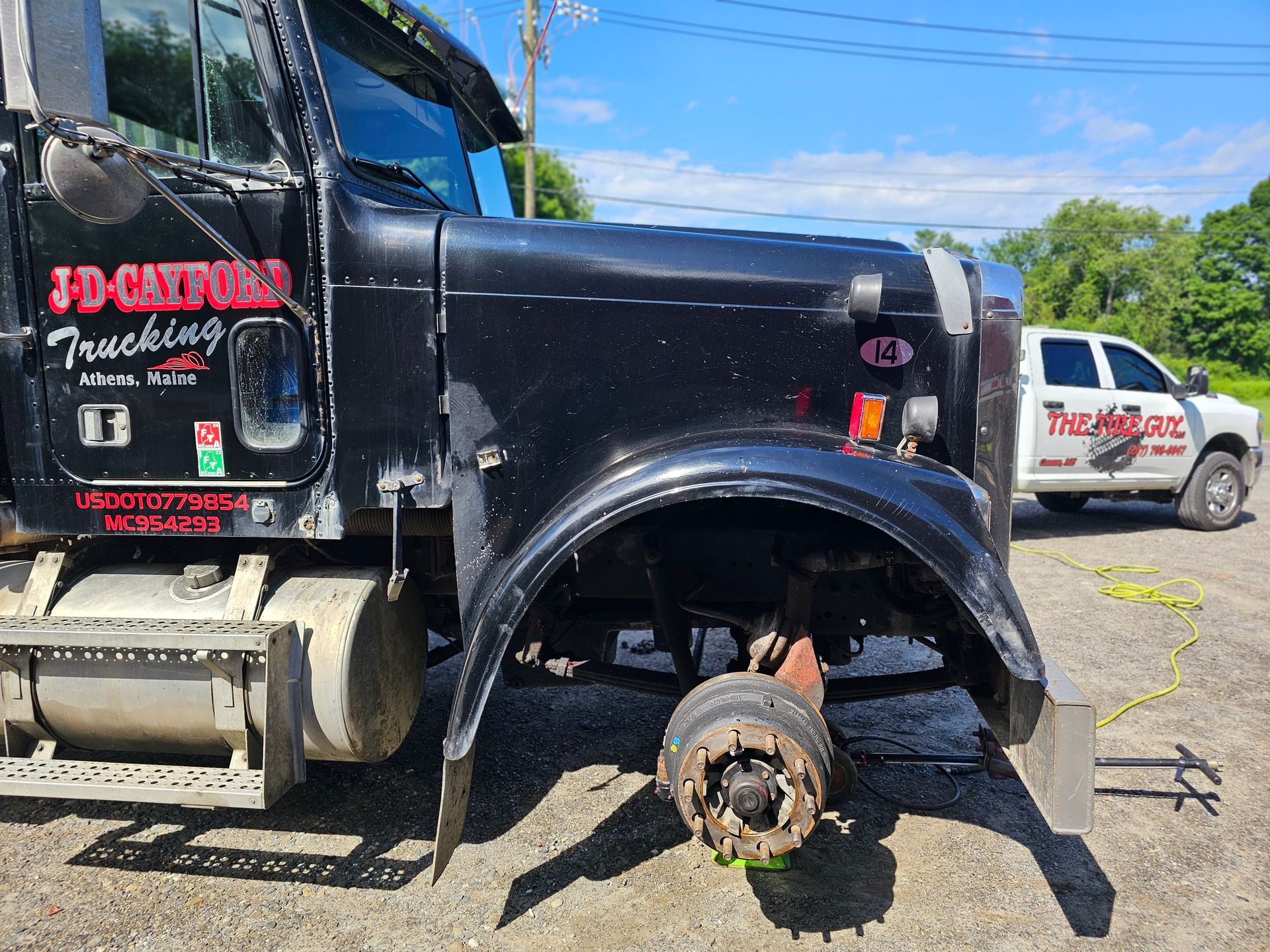 A black semi truck with a broken wheel is parked in a dirt lot.