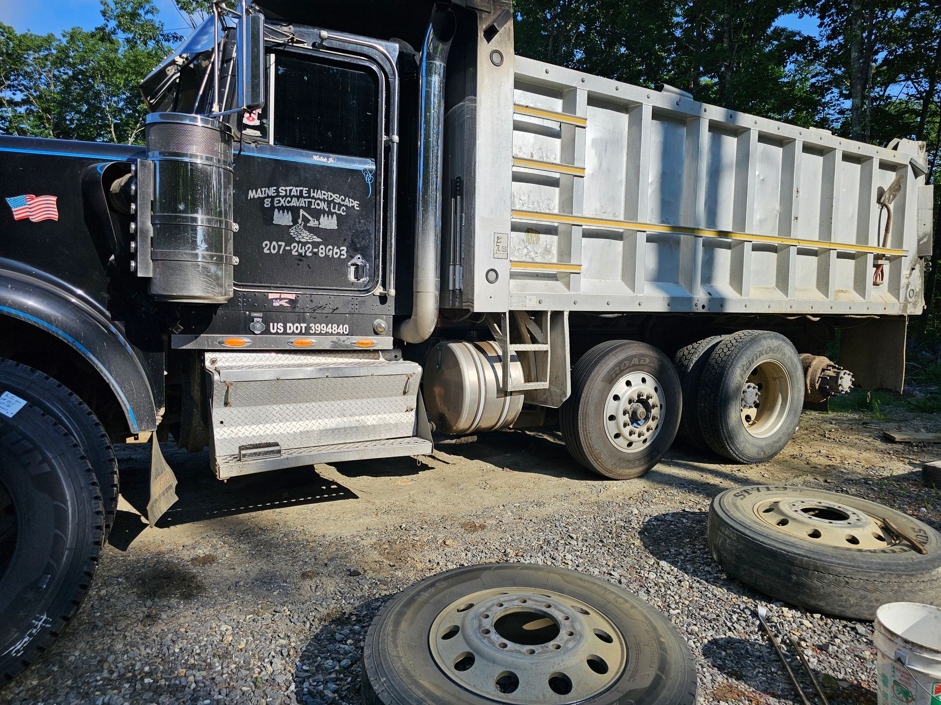 A dump truck is parked in a gravel lot next to some tires.