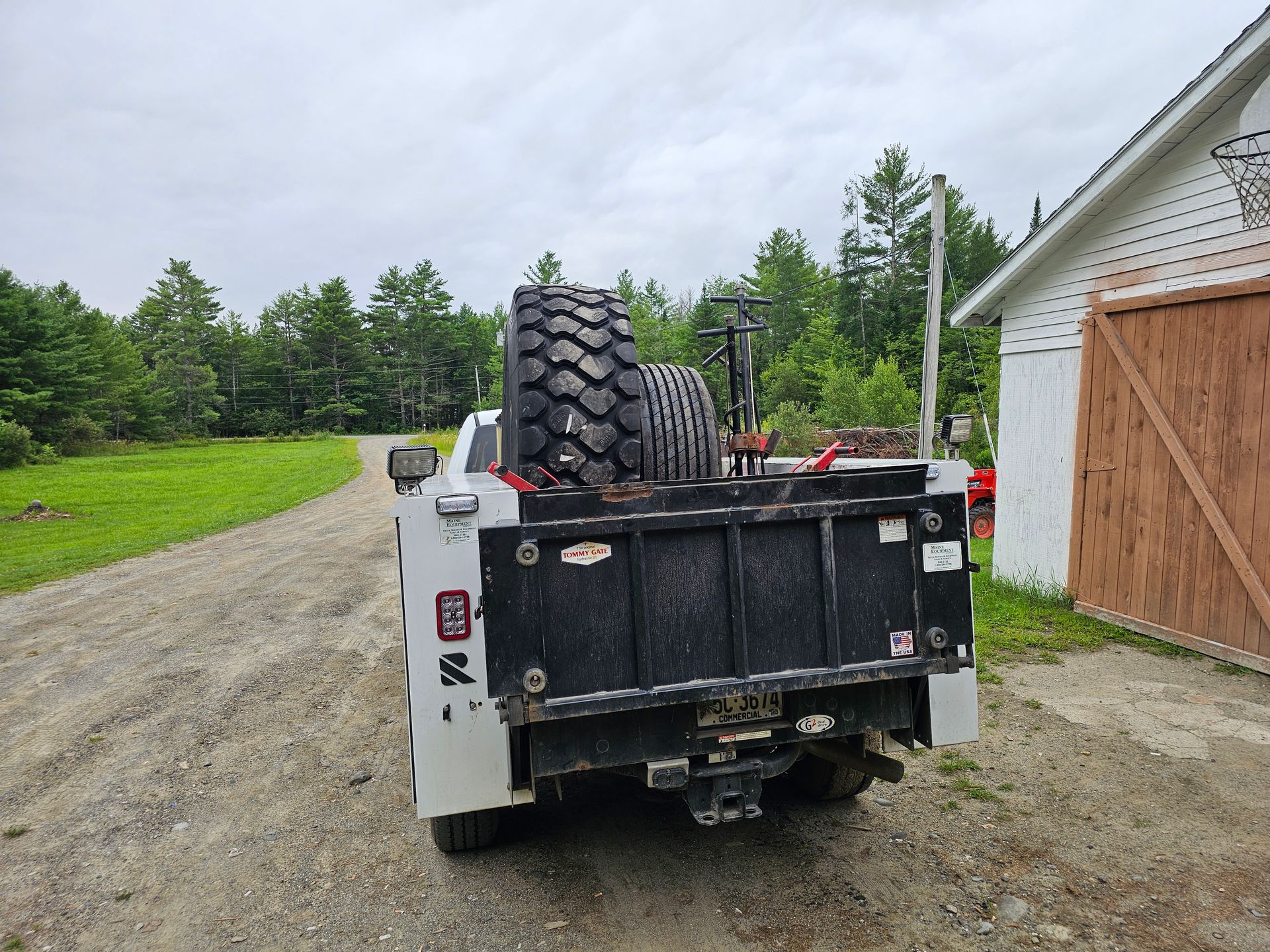 A truck with a tire on the back is parked on a dirt road.