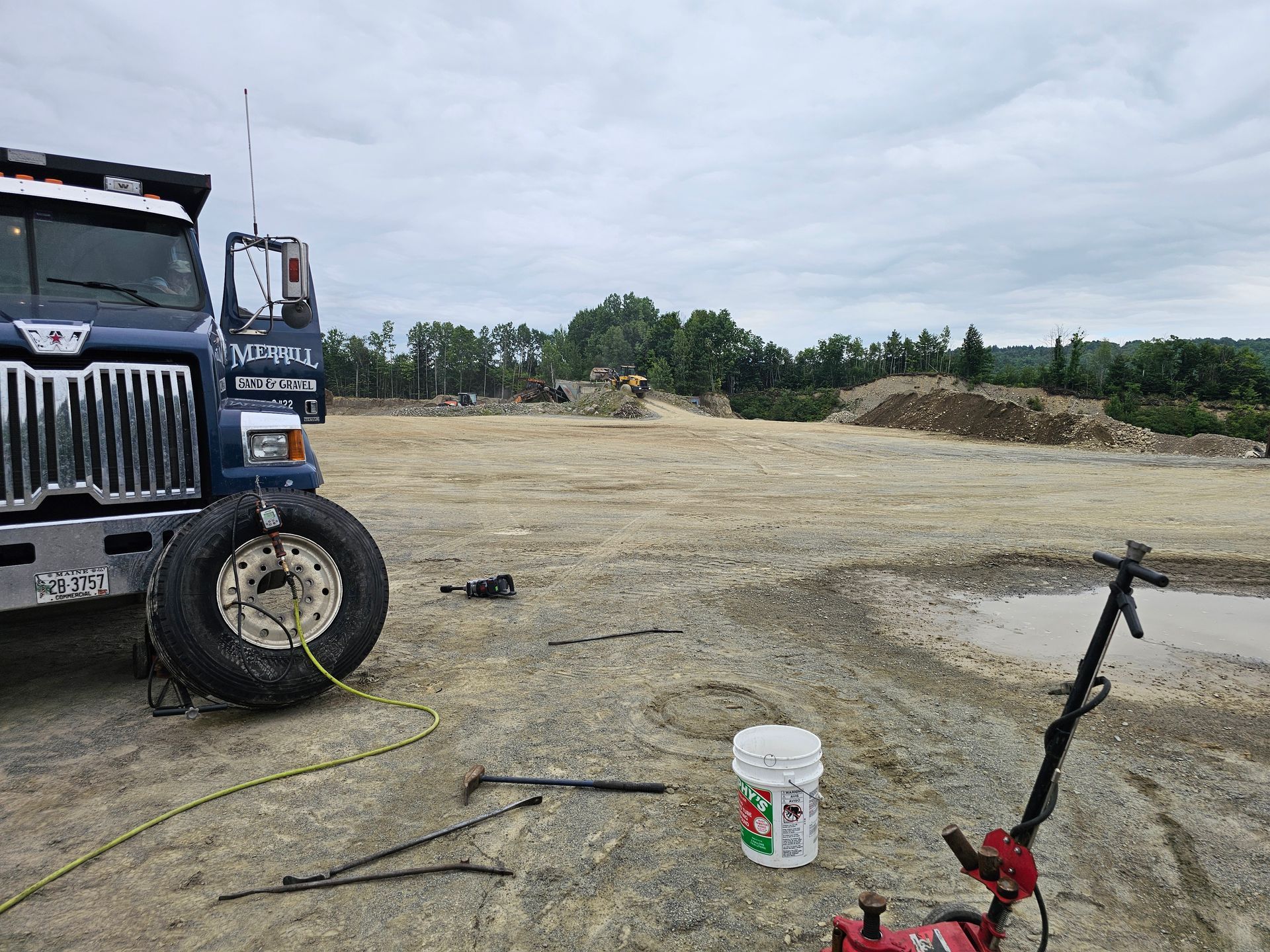 A truck with a flat tire is parked in a dirt field.