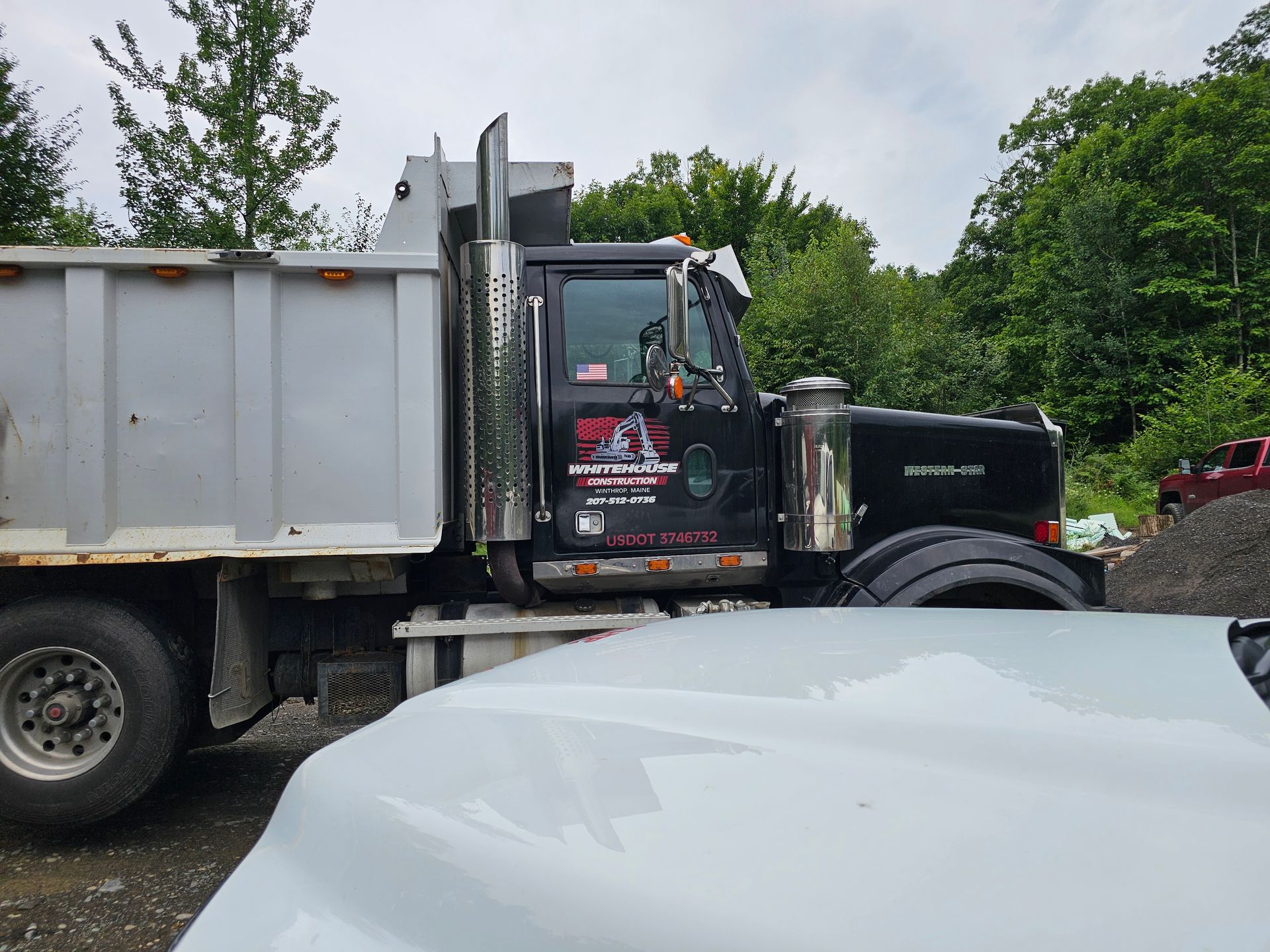 A dump truck is parked next to a white car.