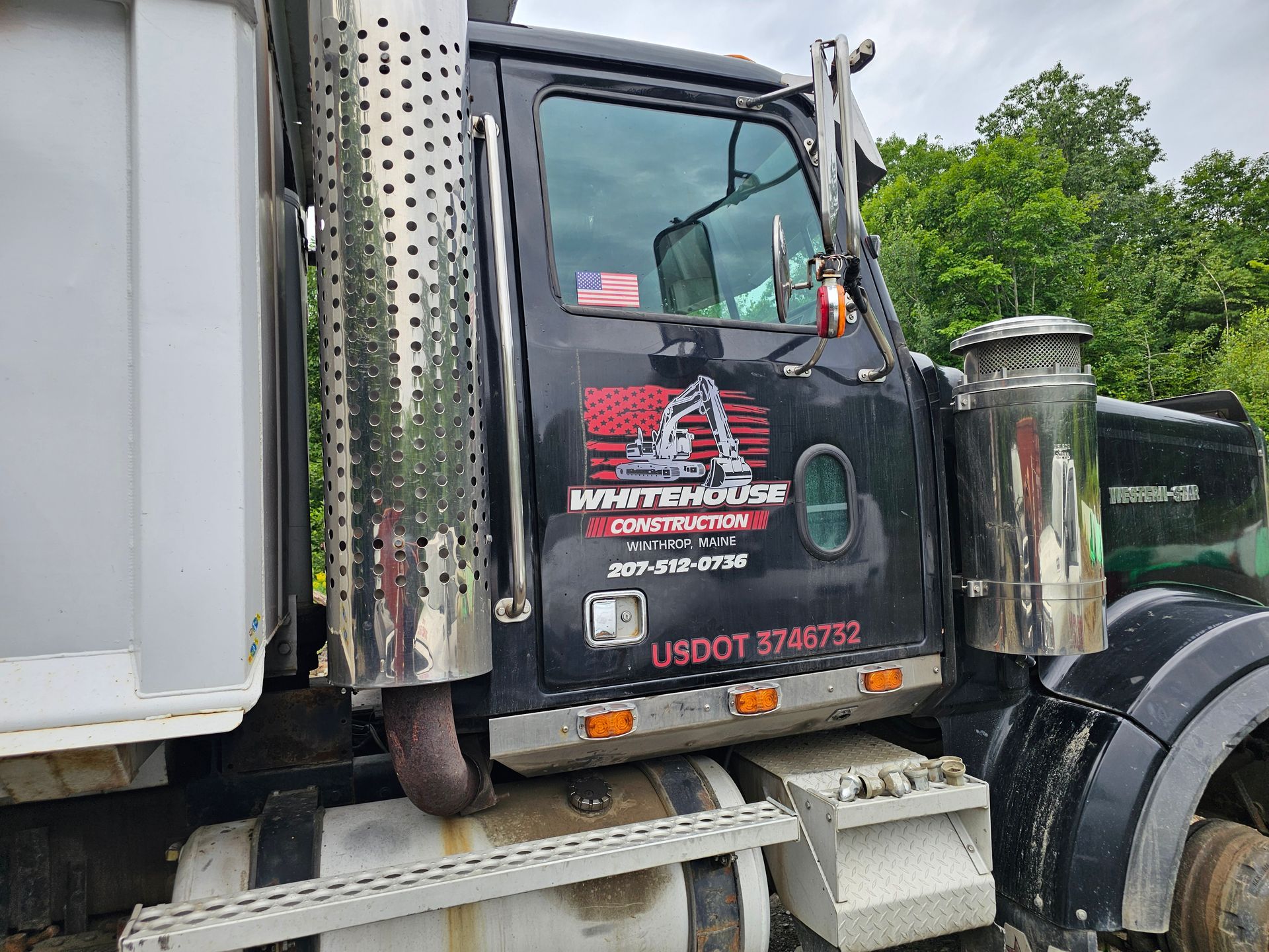 A dump truck is parked in a field with trees in the background.
