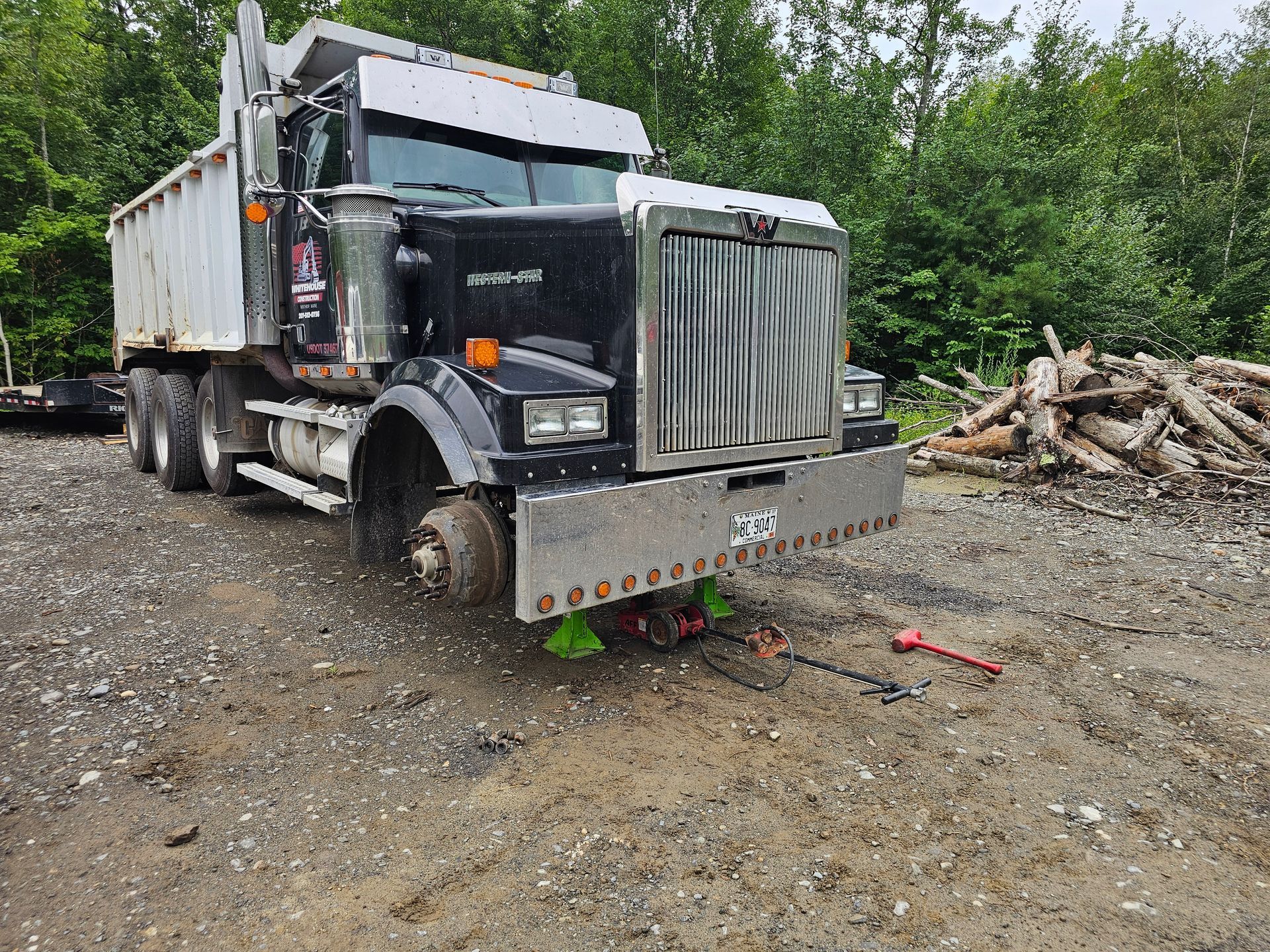 A dump truck is parked in a dirt lot next to a pile of logs.