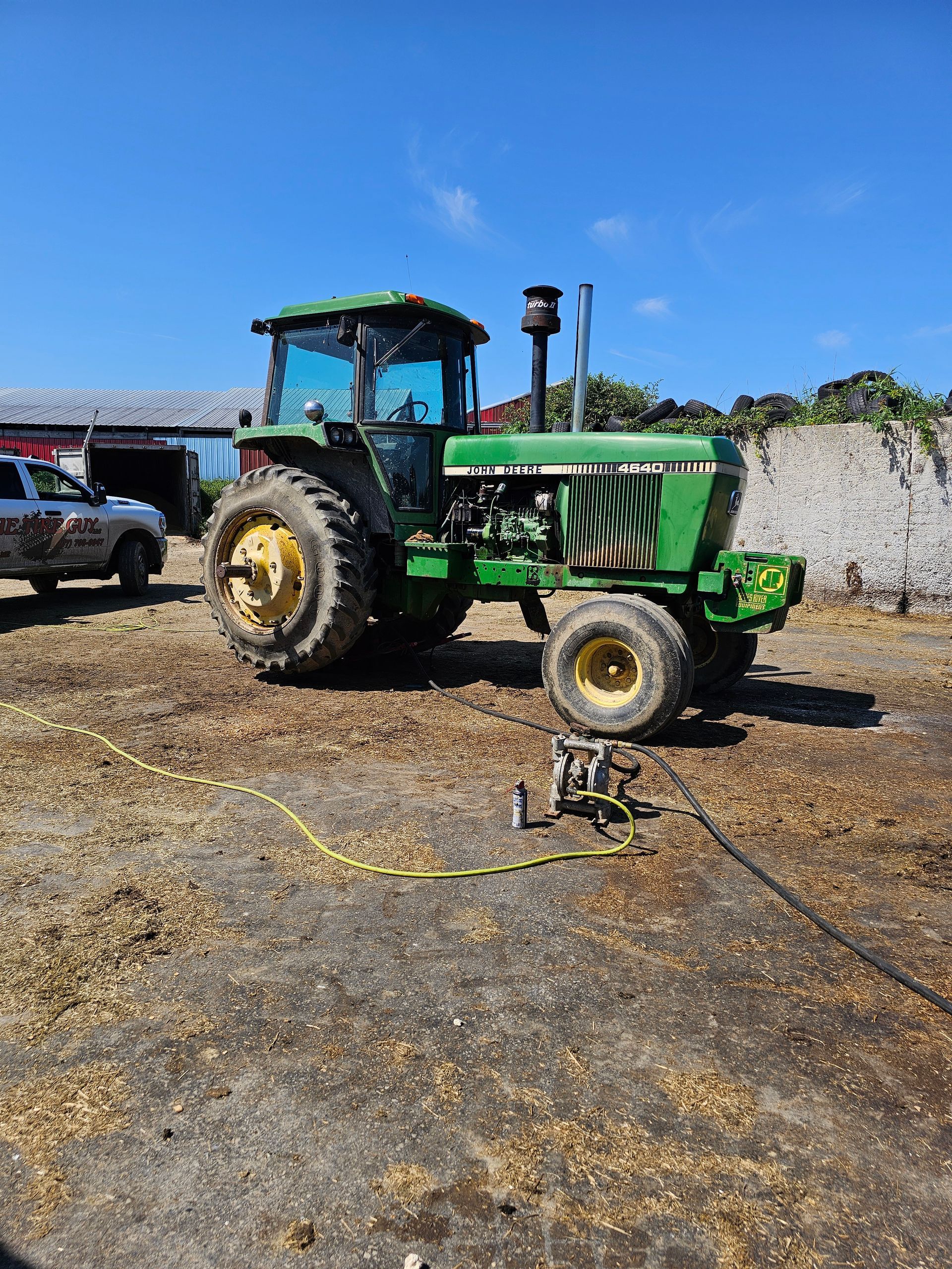 A green tractor is parked in a dirt field next to a white truck.