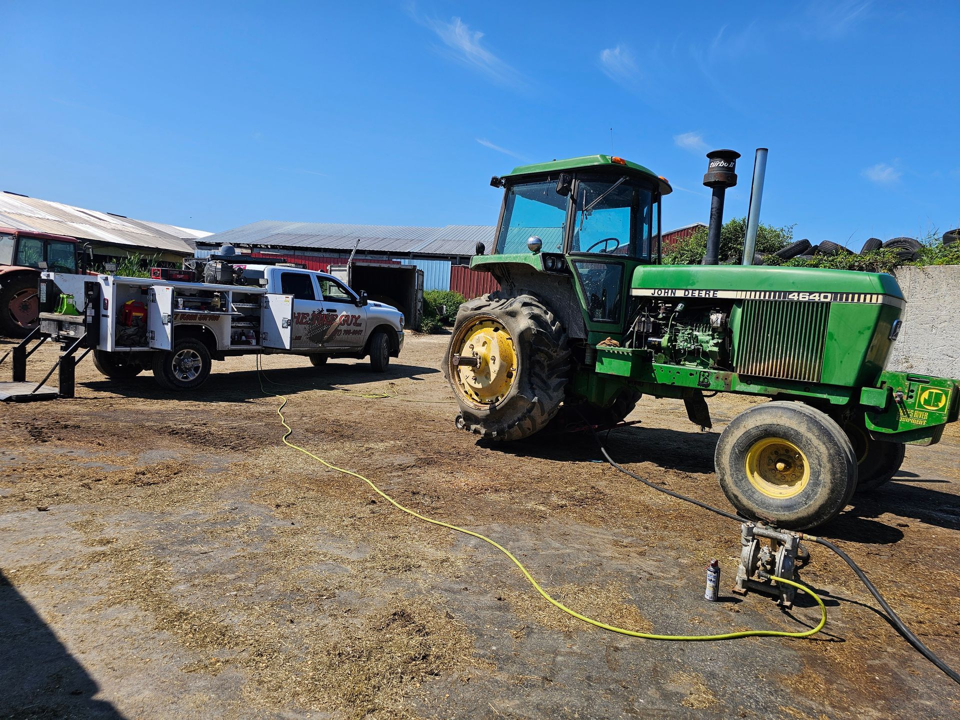 A green tractor is parked in a dirt field next to a white truck.