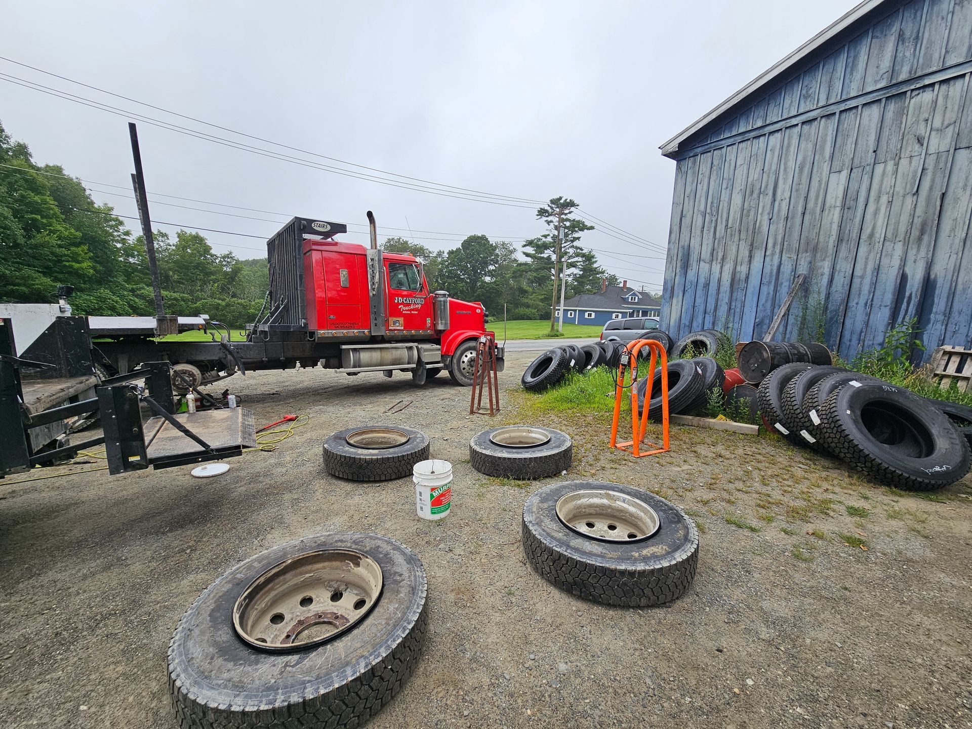 A red semi truck is parked next to a pile of tires.