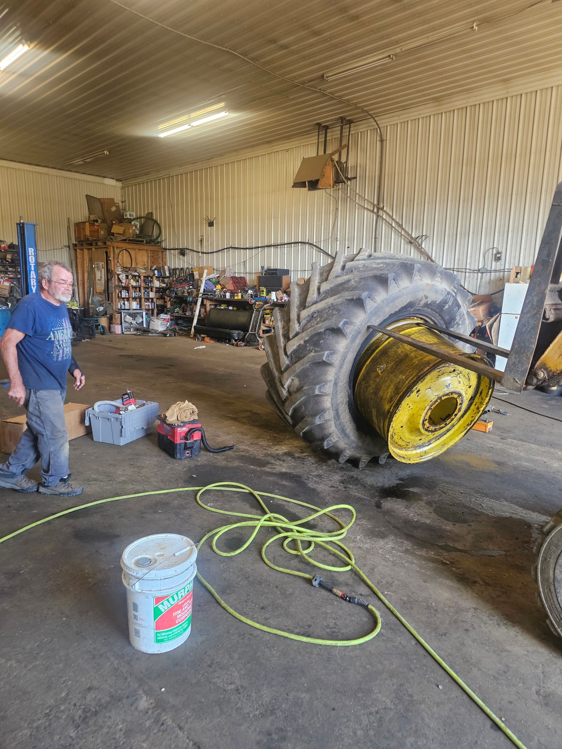 A man is standing next to a large tire in a garage.