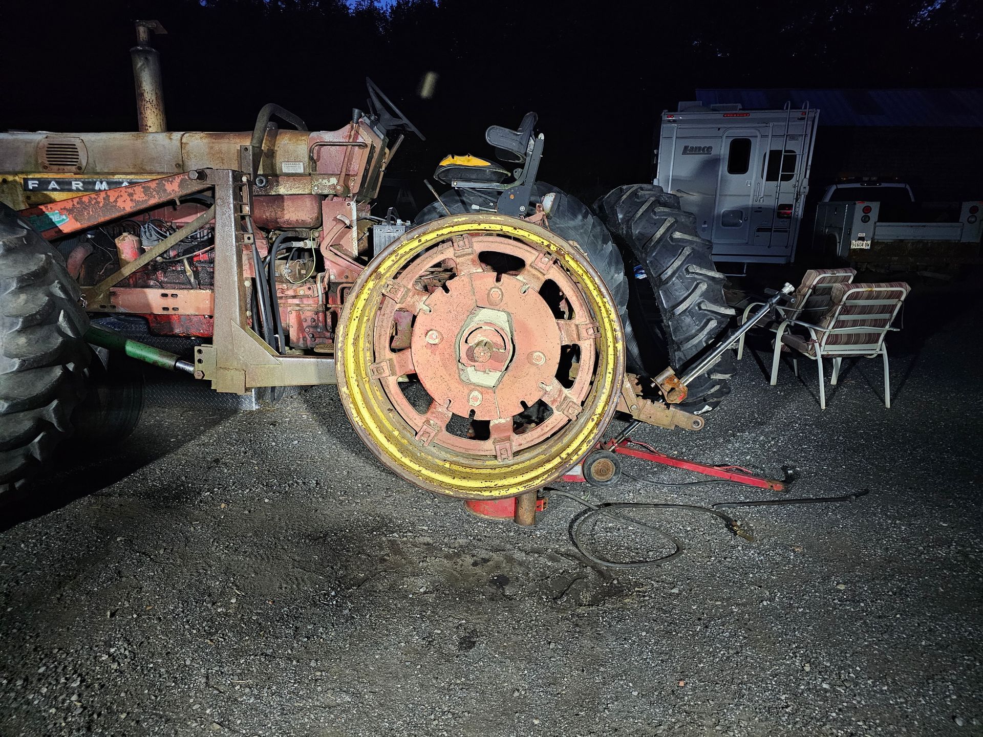 An old tractor is sitting on the ground in a parking lot at night.