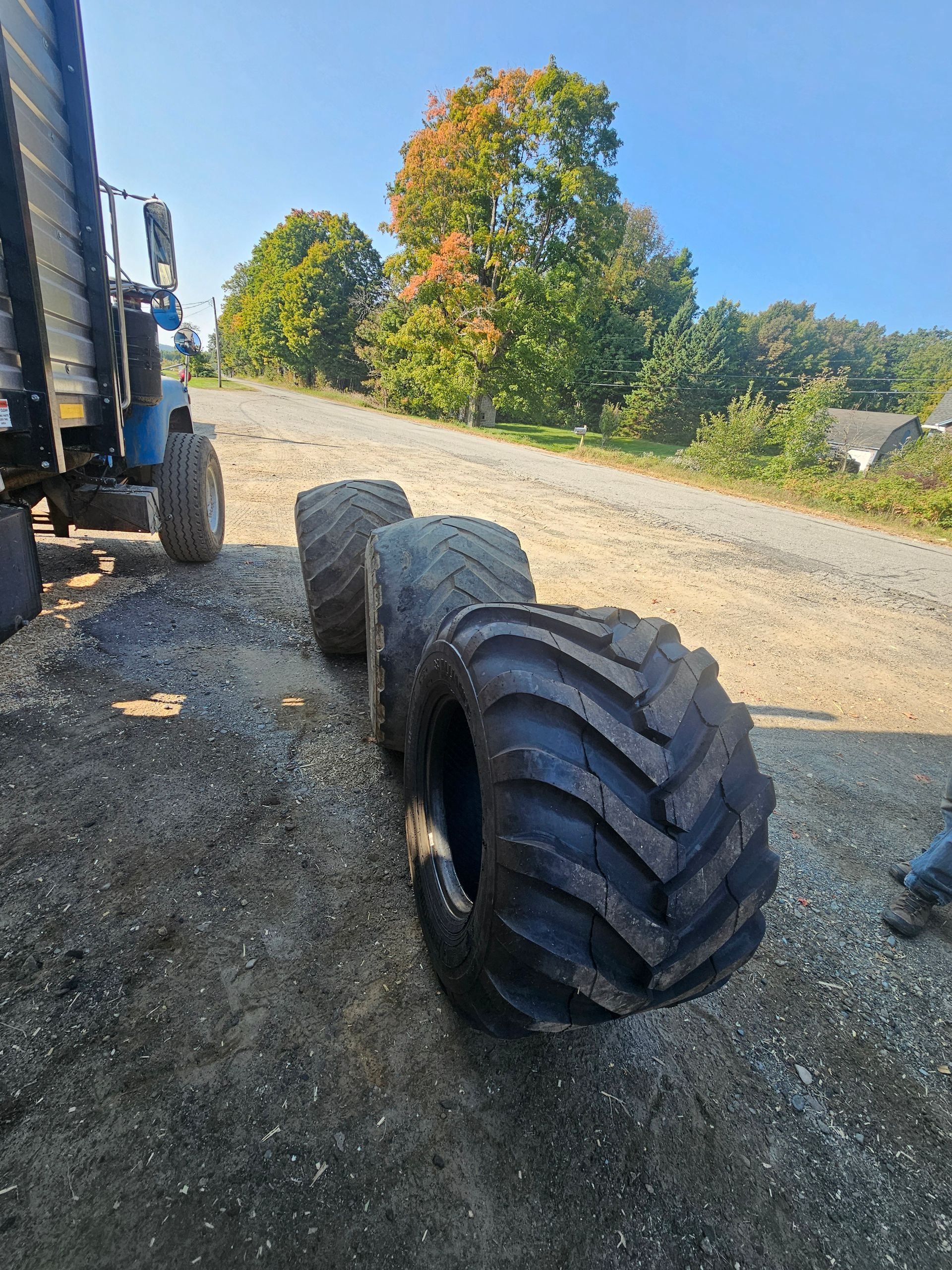 Three tires are sitting on the side of a dirt road.
