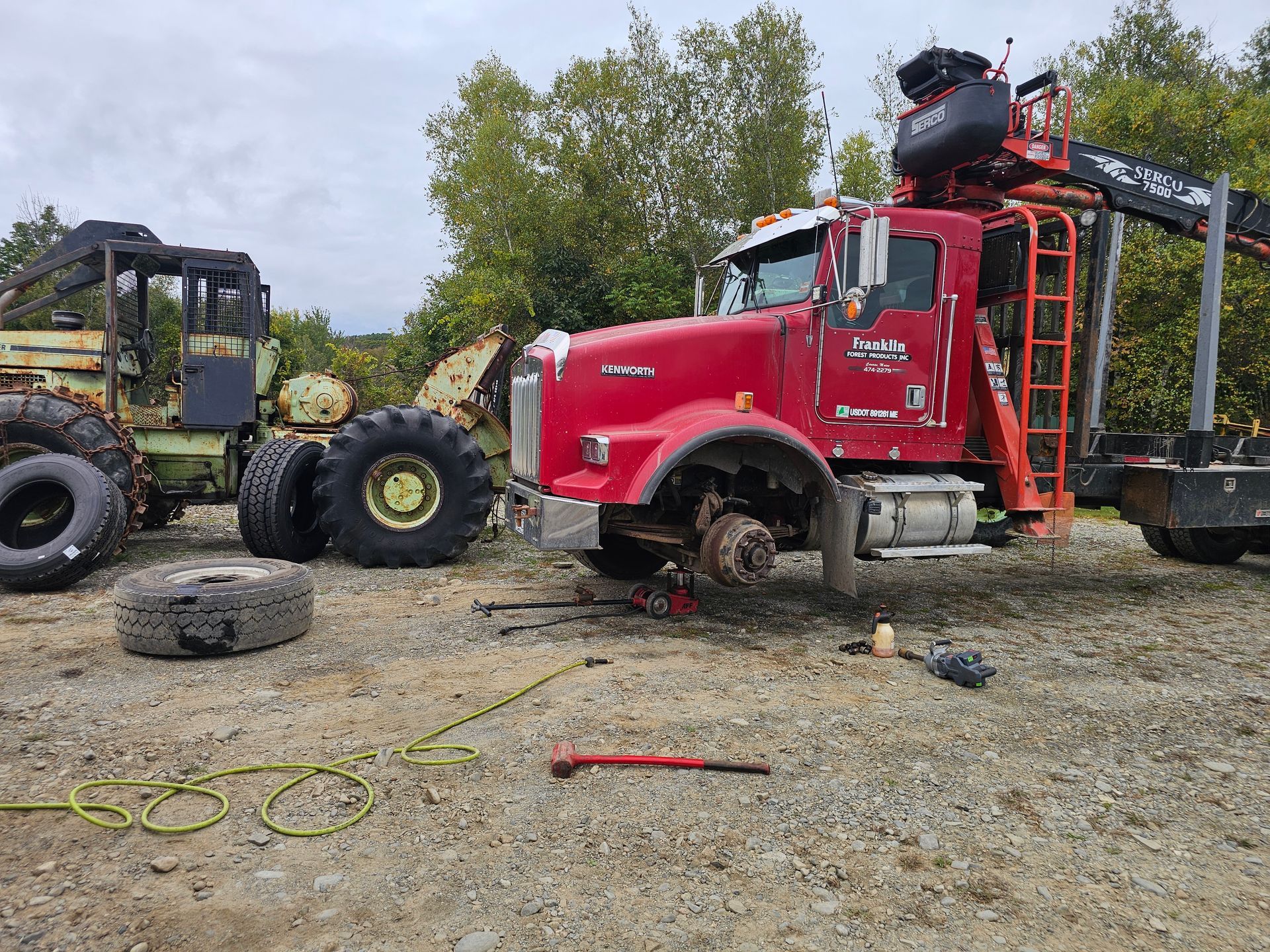 A red truck is sitting in a gravel lot next to a tractor.