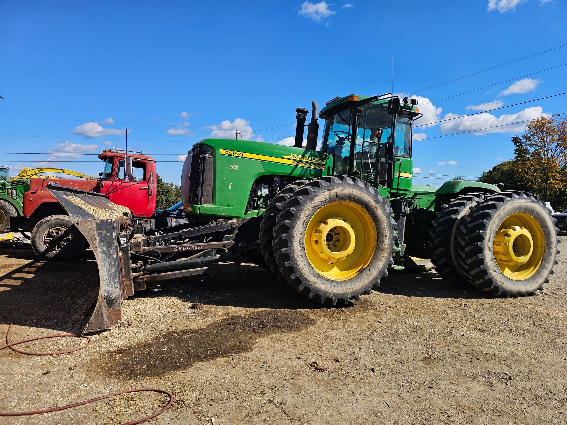 A john deere tractor is parked in a dirt lot next to a red truck.