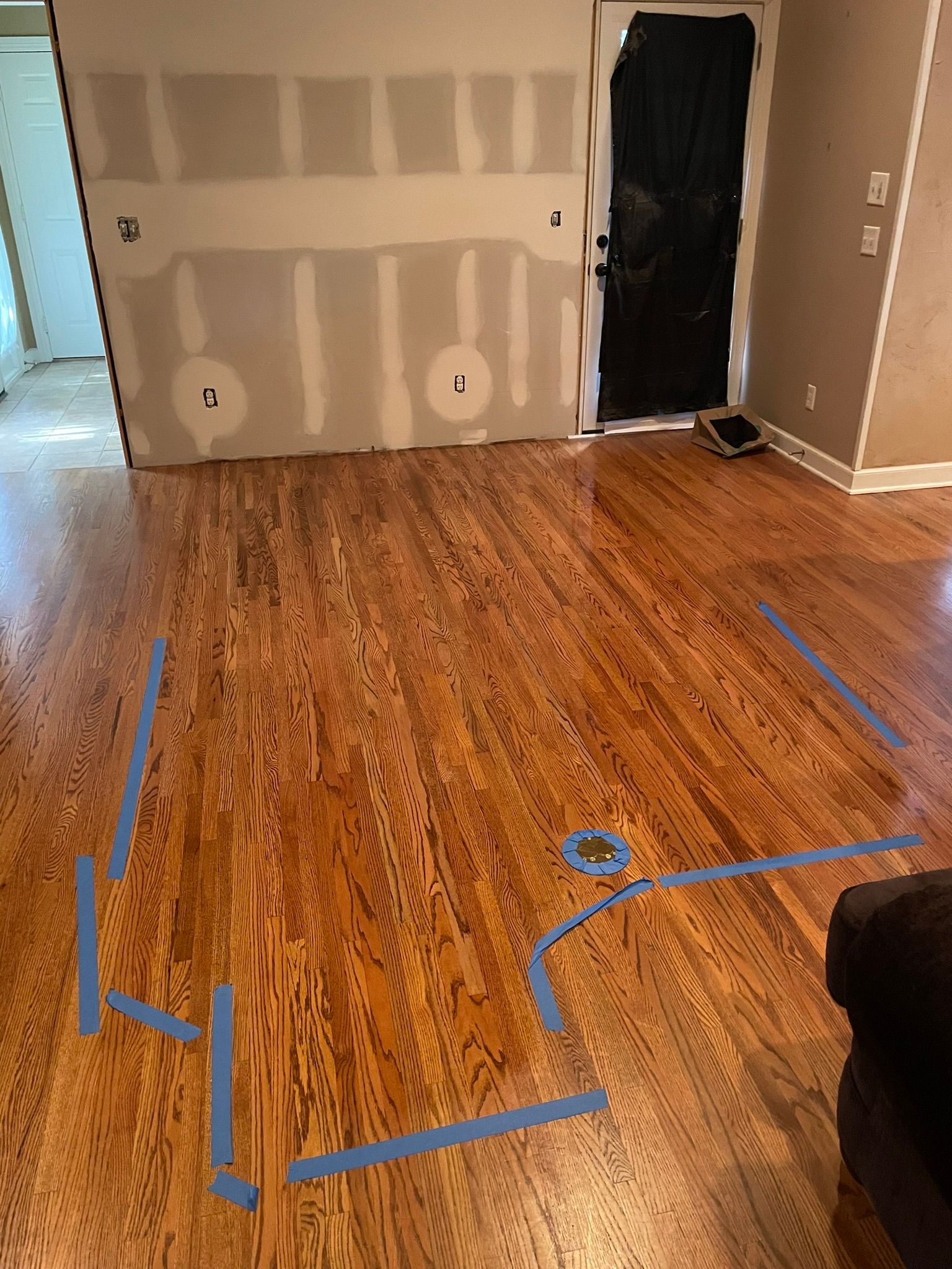 A living room with hardwood floors and blue tape on the floor.