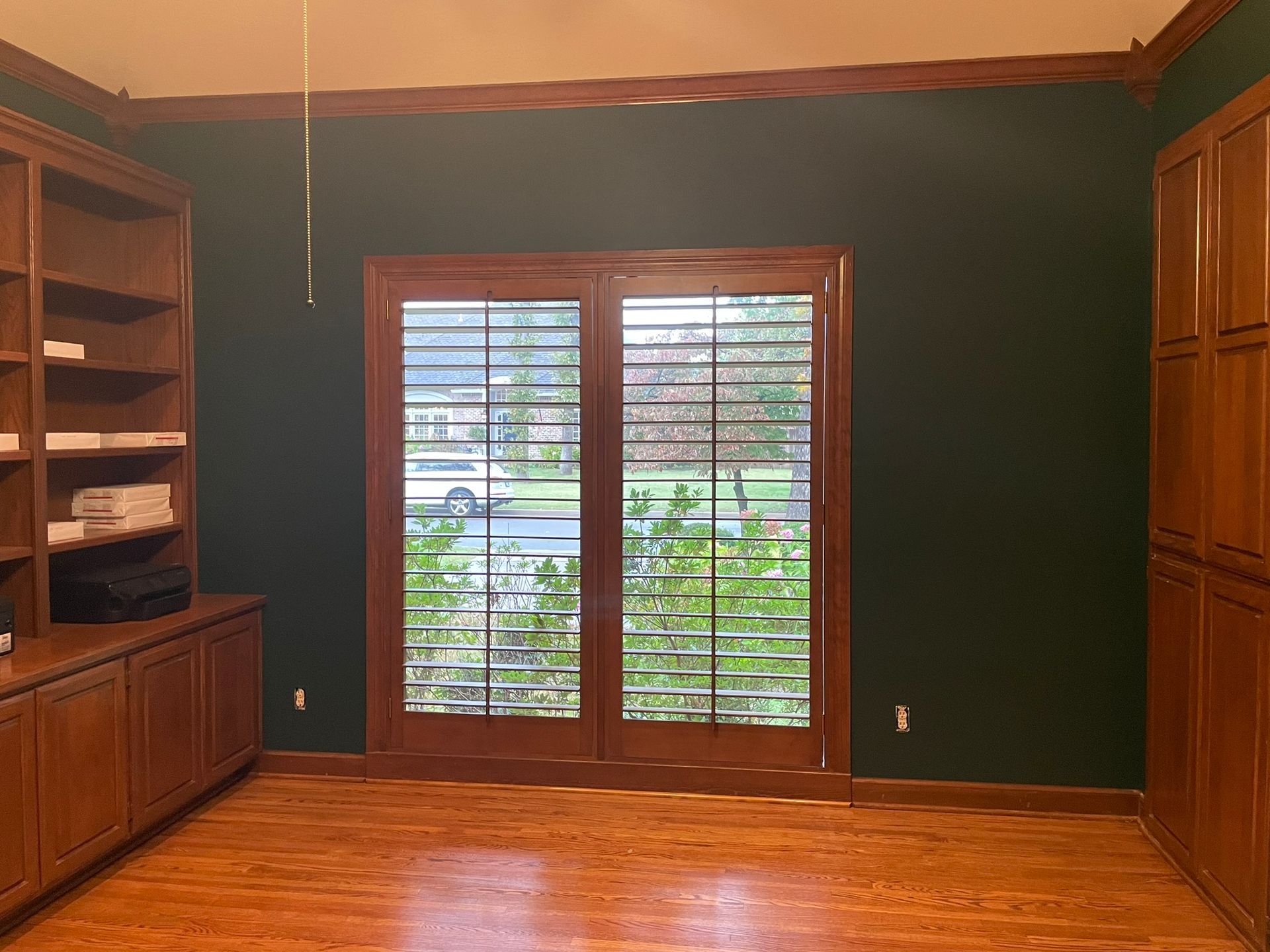 A large empty room with hardwood floors and shutters on the windows.
