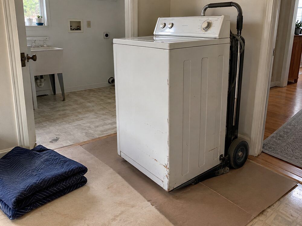 Old washing machine positioned on an appliance dolly for removal.