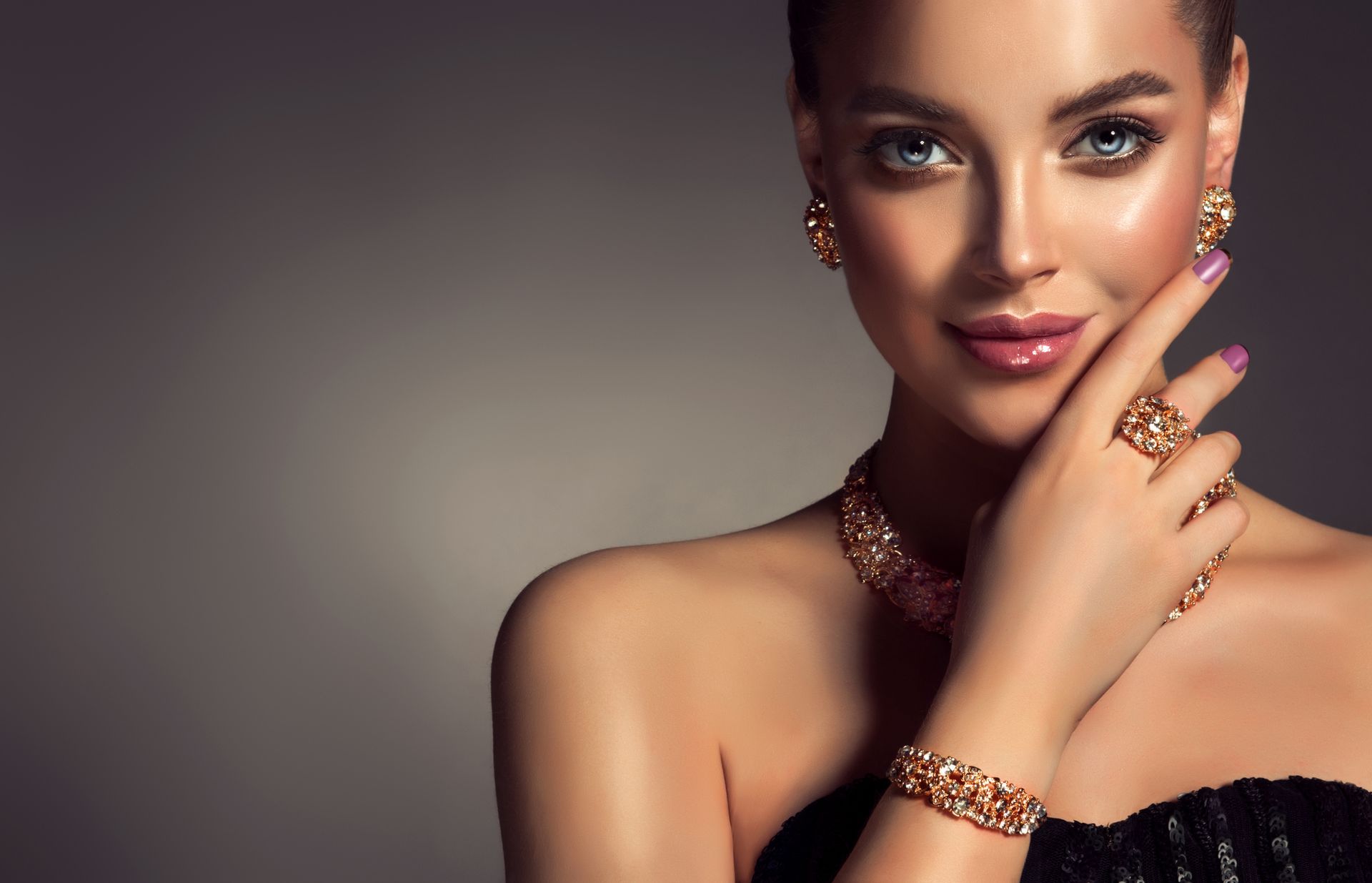 A woman wearing a bracelet and earrings is covering her face with her hand.