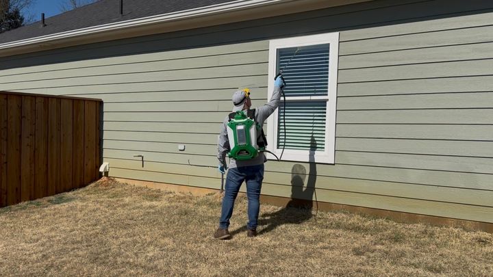 Worker in green jacket painting exterior shutters on a house wall.