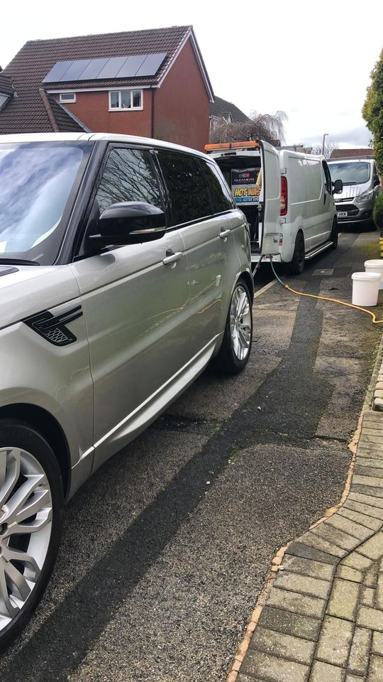 A silver range rover sport is parked in a driveway next to a white van.