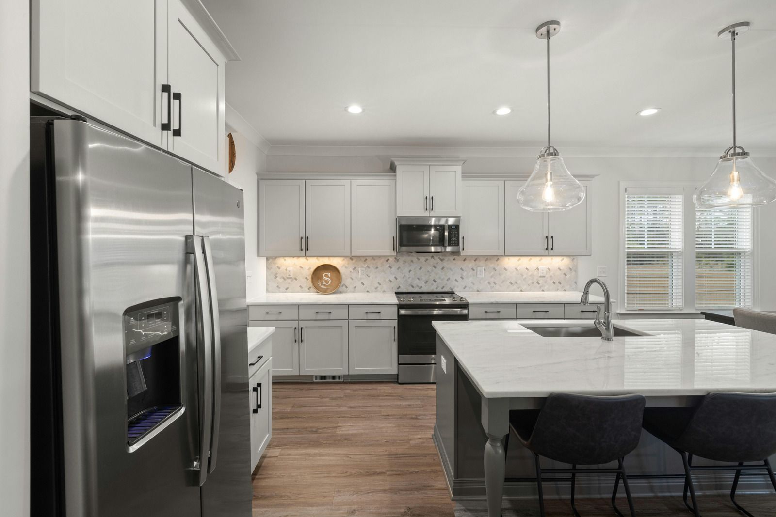 Modern kitchen with stainless steel appliances, white cabinets, large island, and pendant lights
