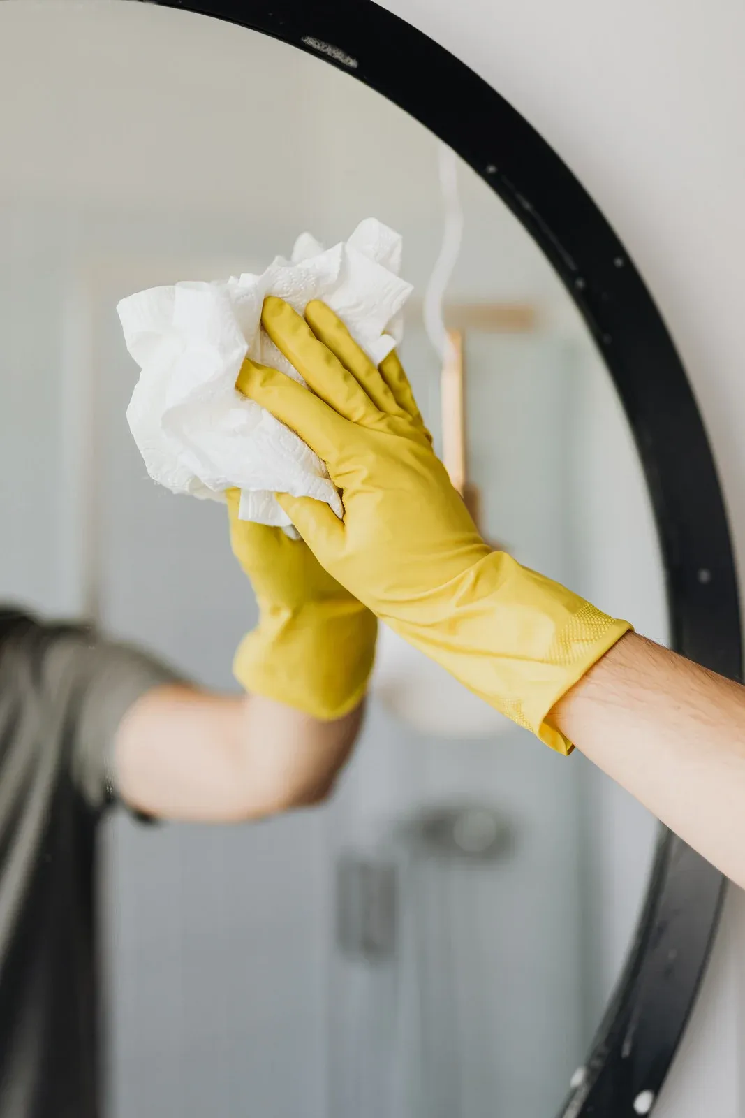 Yellow-gloved hands wiping a bathroom mirror with a white cloth