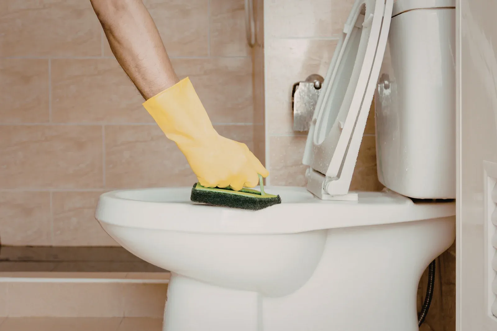 Hand in yellow glove scrubbing a toilet bowl with a sponge in a bathroom