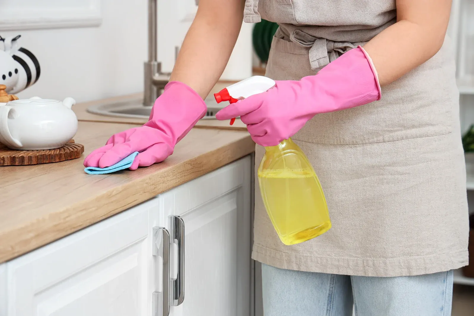 Person wearing pink gloves cleaning a kitchen counter with a spray bottle and cloth