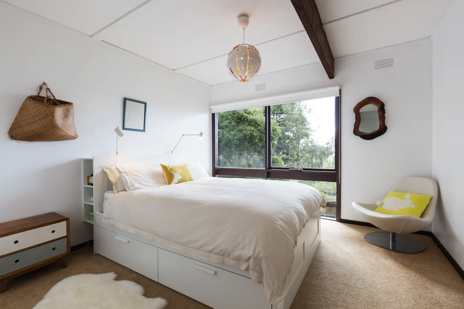 Bright bedroom with a white bed, large window, and modern chair in soft neutral tones