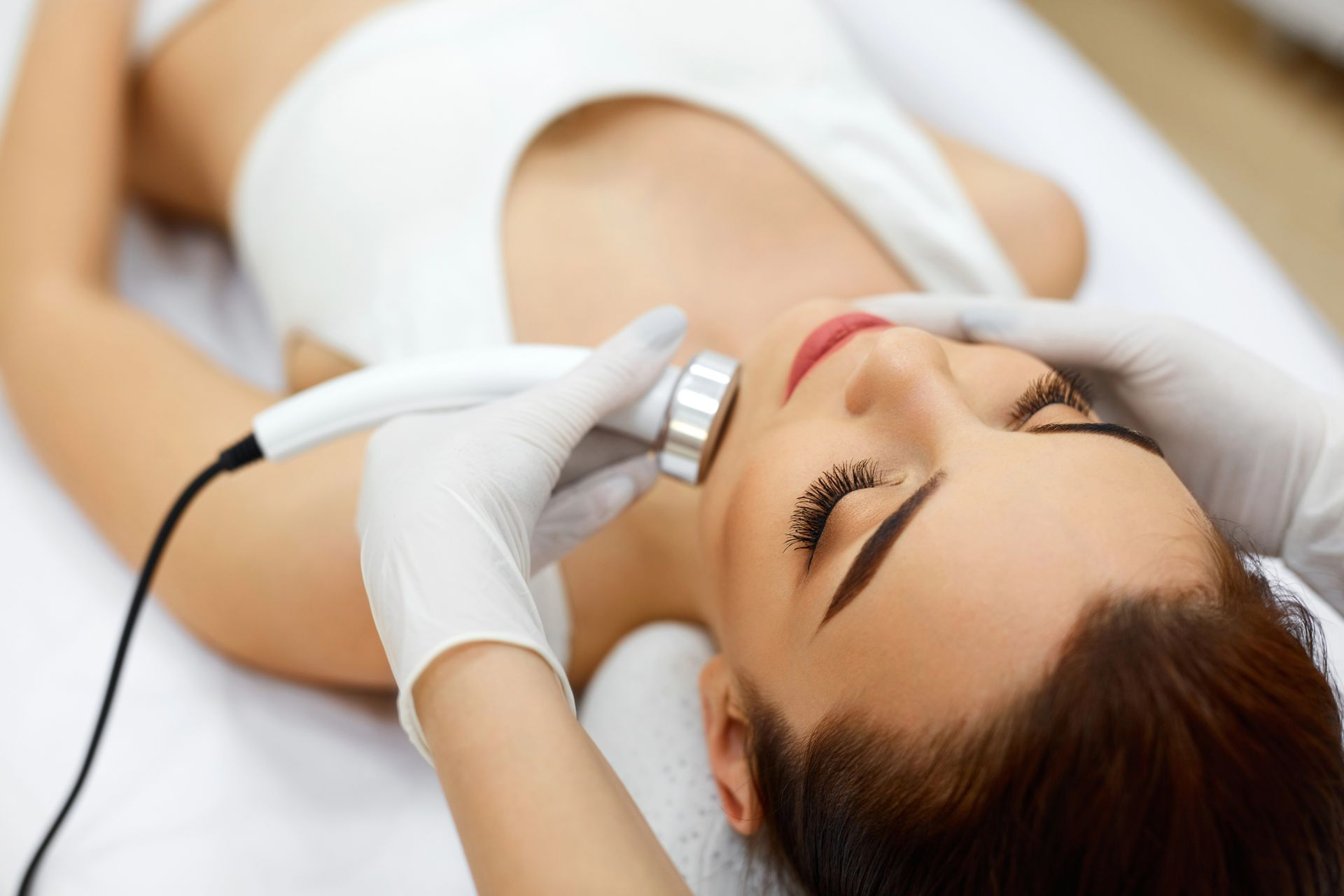 Mujer tumbada en una camilla durante un tratamiento facial con un dispositivo portátil para el cuidado de la piel.