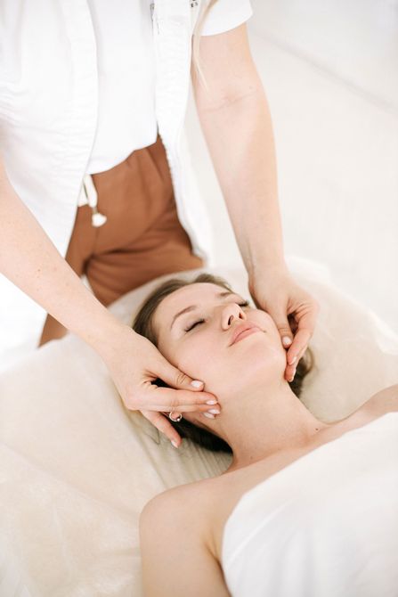 Masajista realizando un masaje facial a un cliente relajado en un entorno de spa.