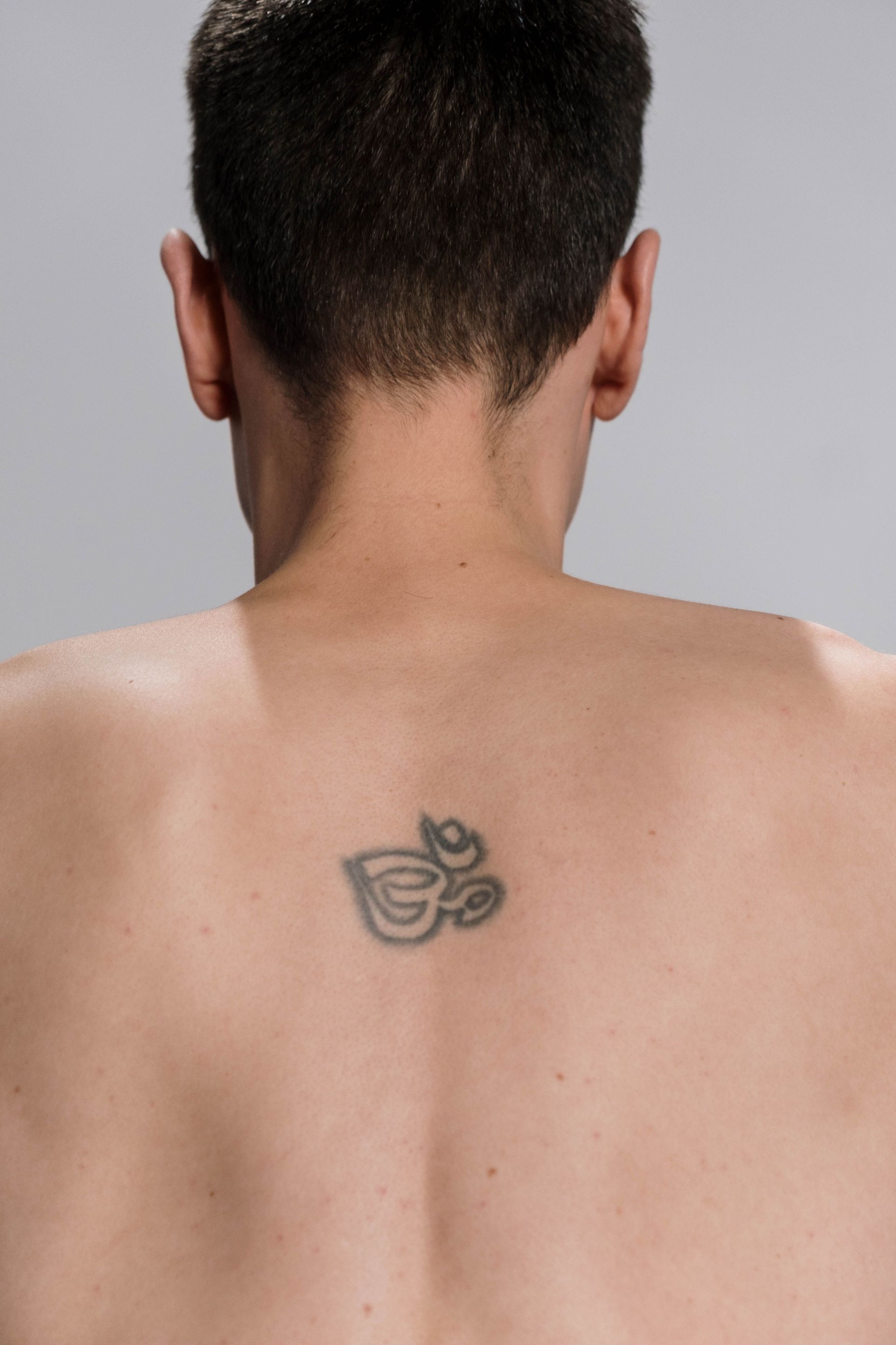 Espalda de una persona con cabello corto y oscuro y un pequeño tatuaje centrado entre los hombros.