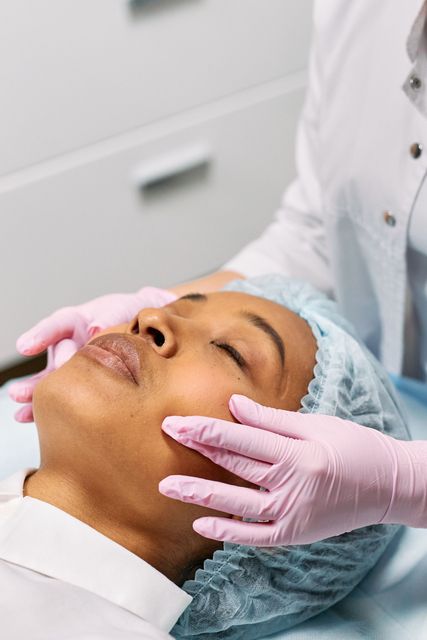 Tratamiento facial de spa con manos enguantadas de rosa masajeando el rostro de una mujer.