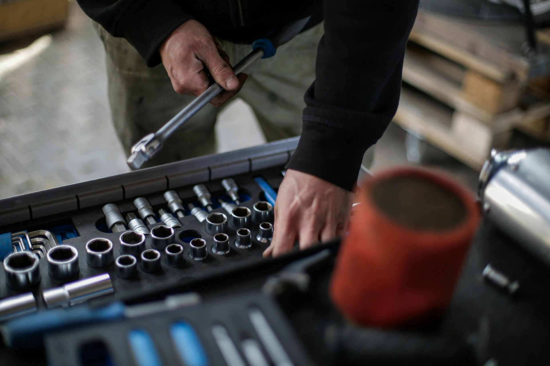 Hands using a ratchet on a socket set in a workshop tool tray
