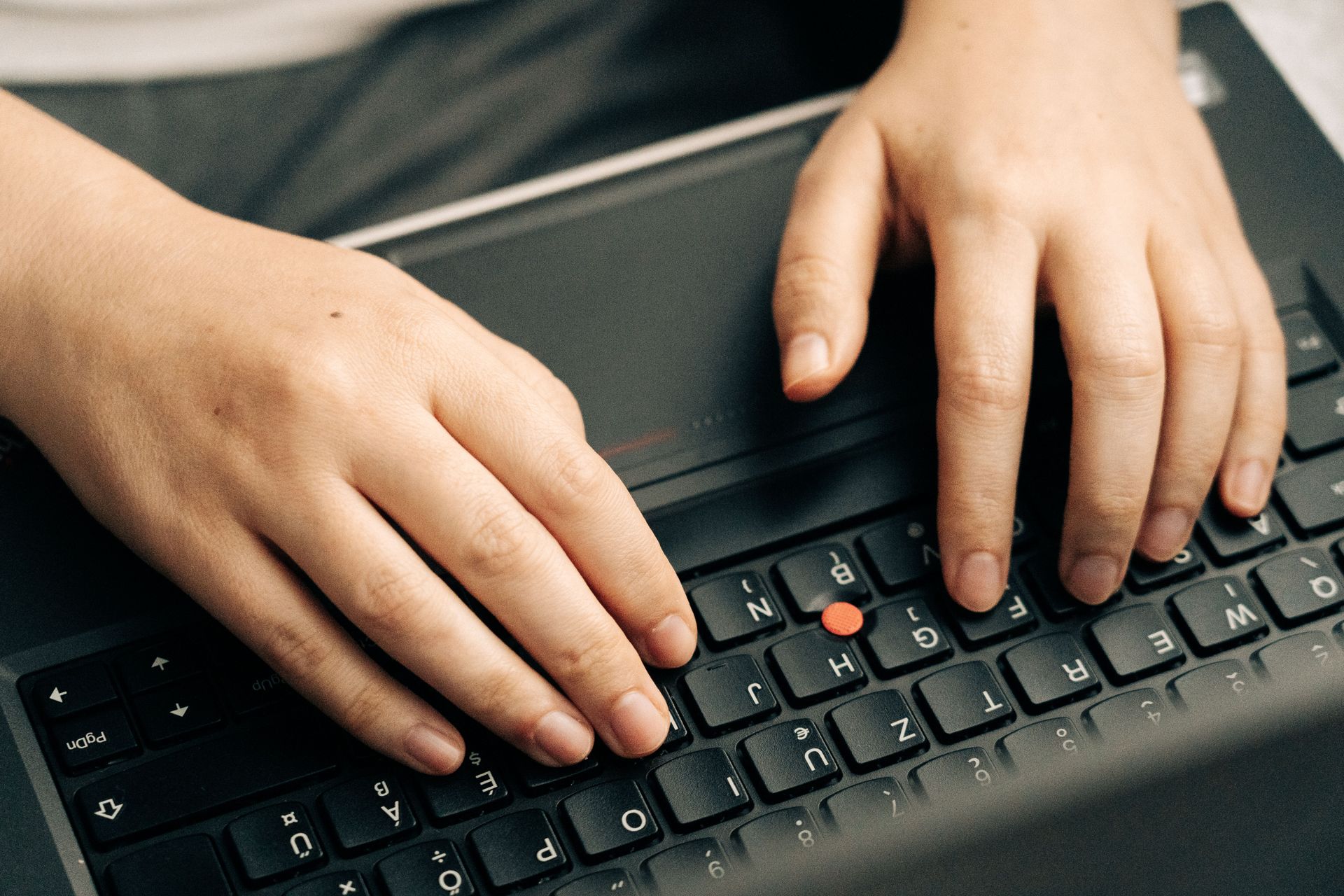 Hands typing on a black keyboard near a red TrackPoint button