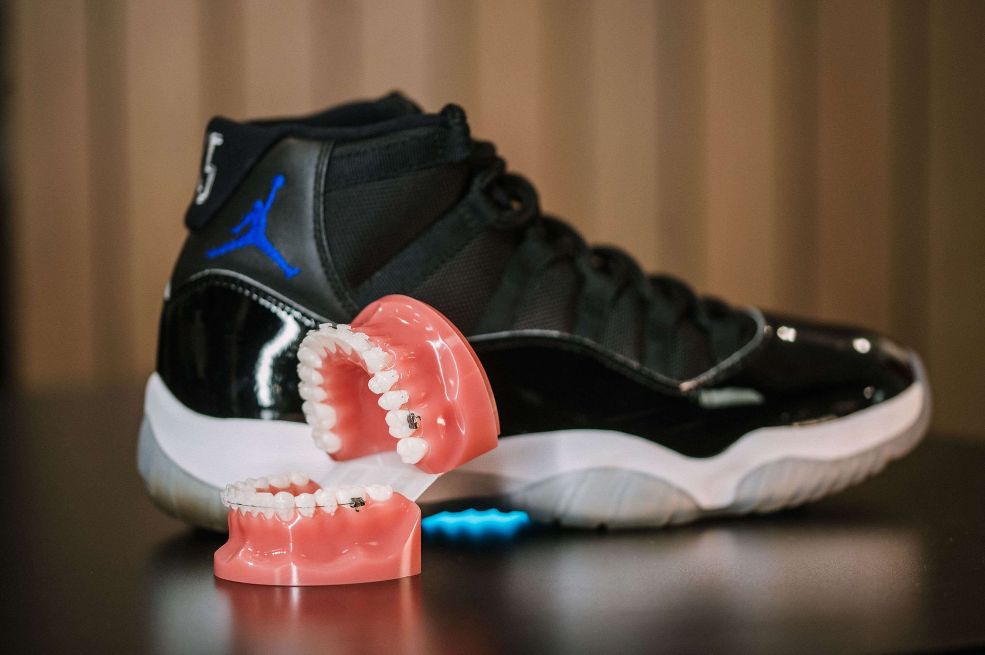 Black Air Jordan sneaker with a pink mouthguard prop on a tabletop, against a blurred brown background