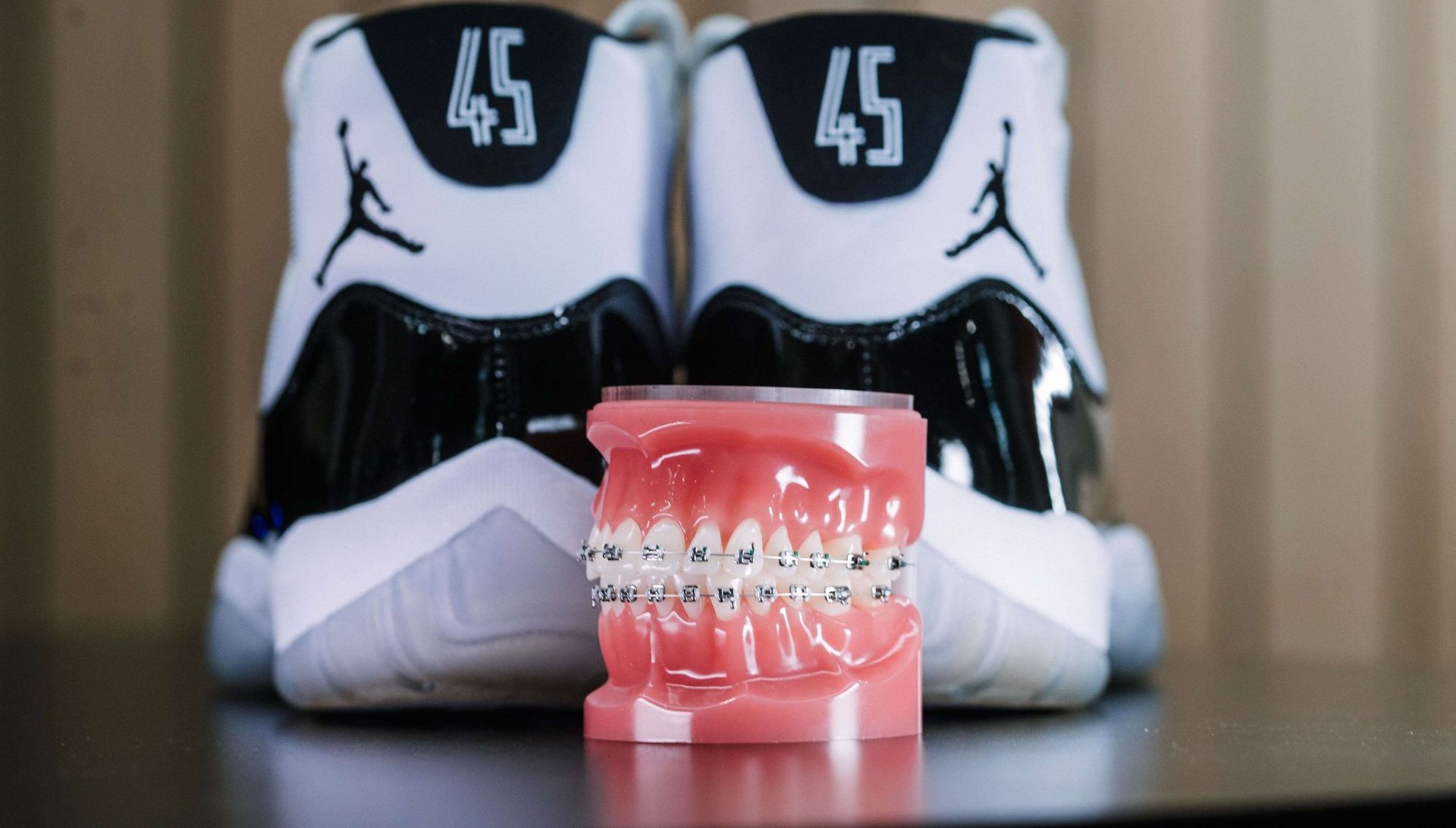 Pink dentures in front of black-and-white sneakers with the number 45 on a table