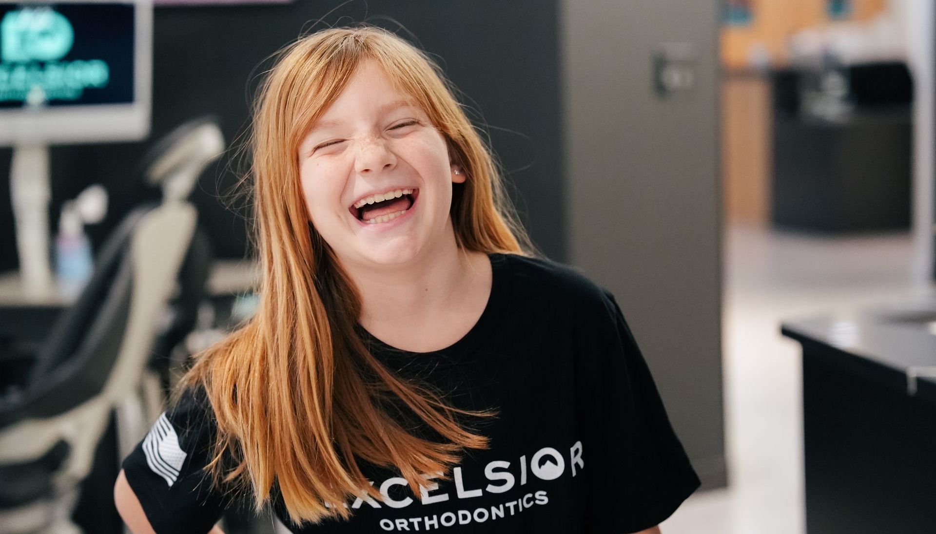 Smiling person in a black T-shirt laughing indoors near an office or store counter