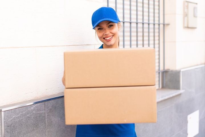 A delivery woman is holding a stack of cardboard boxes.