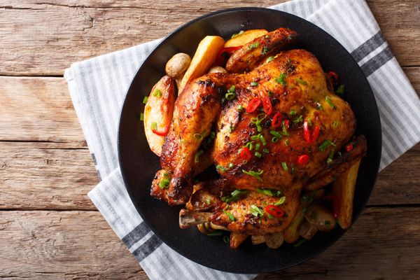 Baked whole chicken with mushrooms and potatoes close-up on a plate on a table. Horizontal top view from above