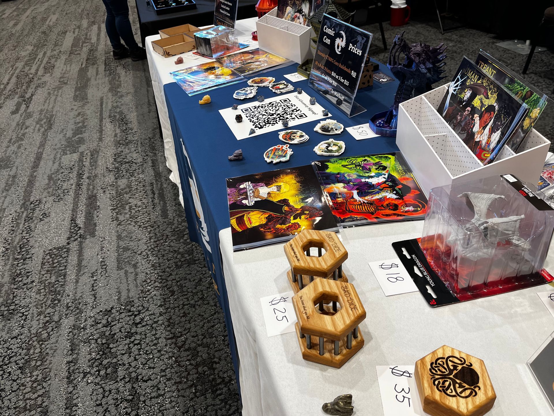 2025 DnD Gifts for the Holidays A table at a convention showcasing board games, dice, and art