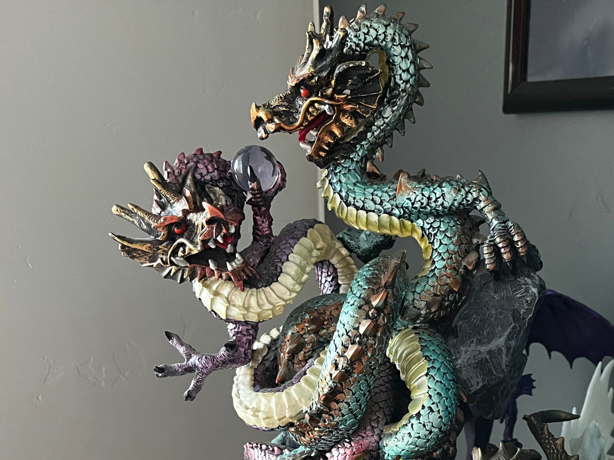 Detailed statue of three-headed dragon in teal, purple, and gold.  Heads snarling, clutching a crystal on a grey base.