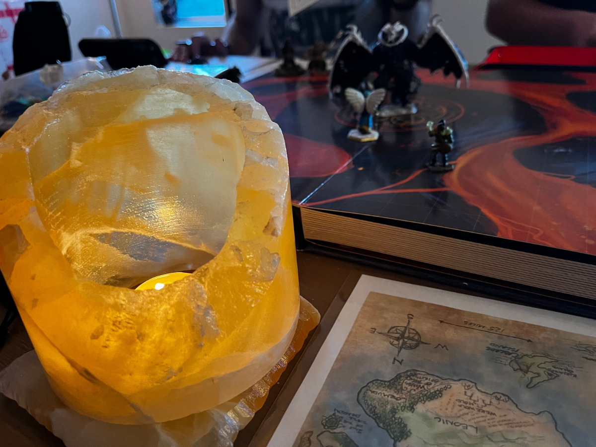 Lit candle in a carved, amber-colored skull. D&D game setting: map, book, and figurines on table.