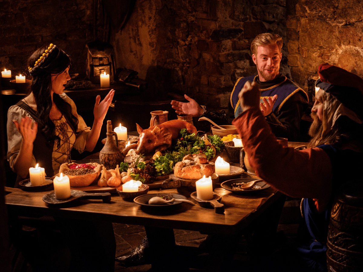 People at candlelit medieval feast. Pig roast on the table.