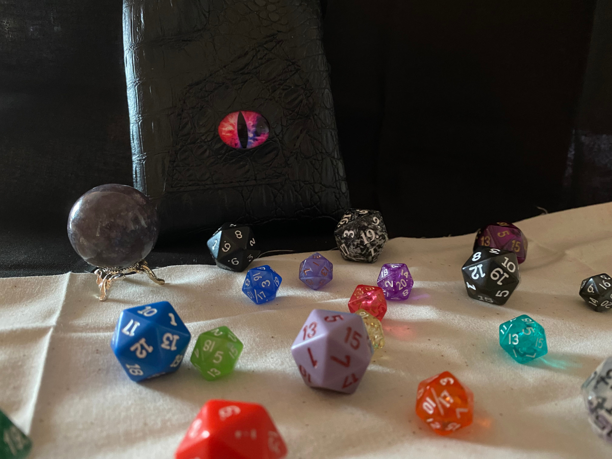Dice of various colors scattered on a white cloth, a purple crystal ball, and a black bag with a red eye.