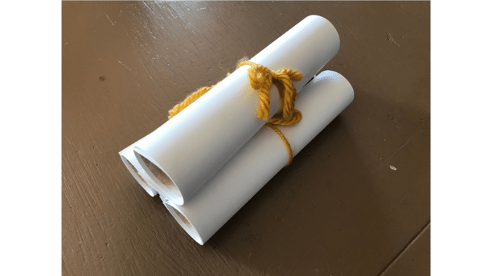 Three white rolled paper tubes bound with yellow string on a brown surface.