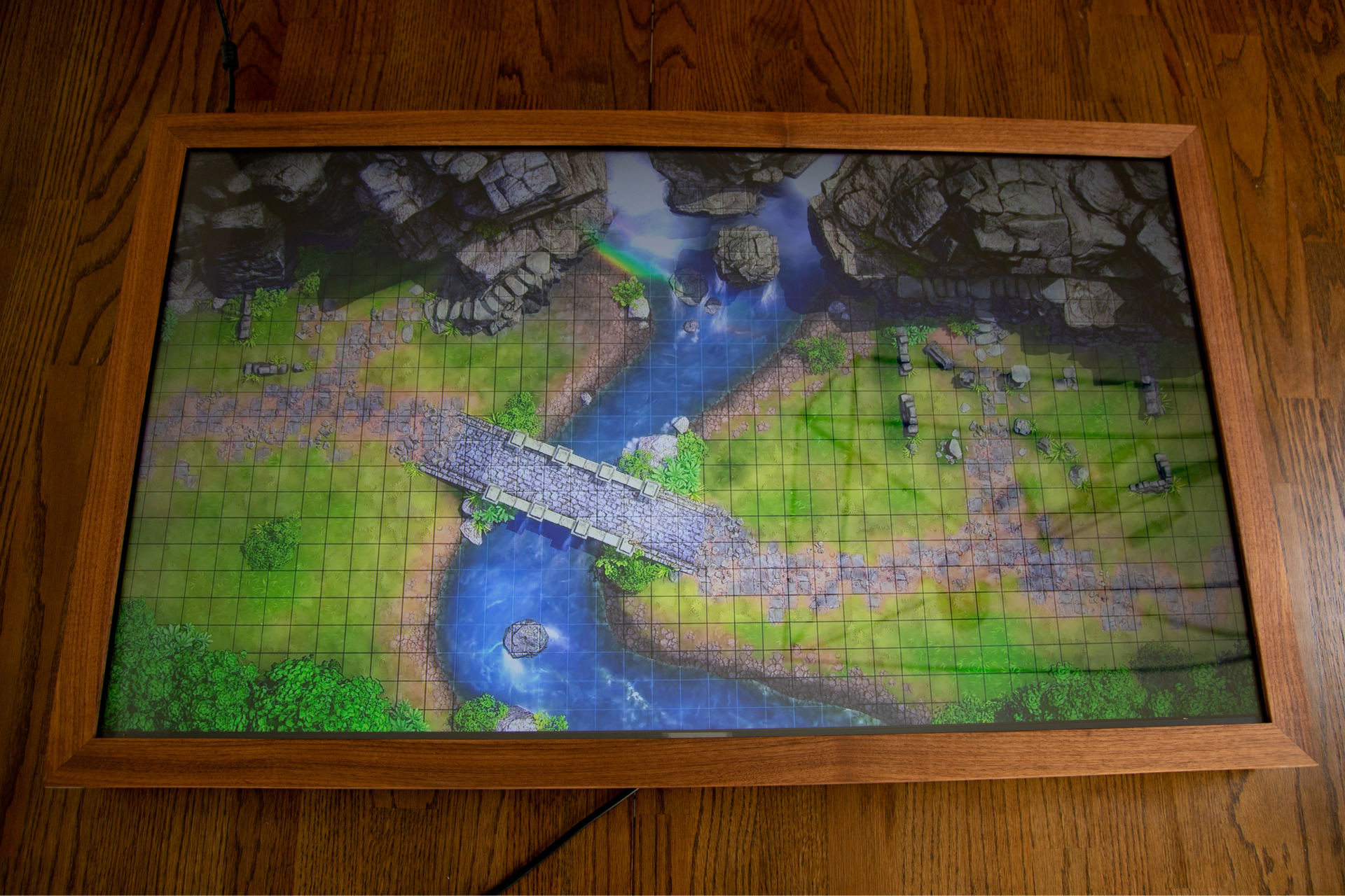 Top-down view of a river and bridge on a digital table, set into a wooden frame.