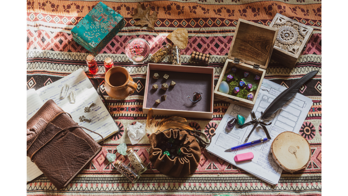 Assortment of tabletop roleplaying game items on a patterned fabric: dice, boxes, notebooks, quill pen, and trinkets.